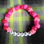 Pink beaded bracelet with 'SLAYER' letters on a plaid fabric background