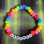 Colorful beaded bracelet with 'RAMONES' charm on a plaid fabric background