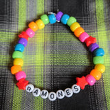 Colorful beaded bracelet with 'RAMONES' charm on a plaid fabric background