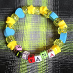Colorful beaded bracelet with letter beads spelling 'KRYSTYNA' on a plaid fabric background.