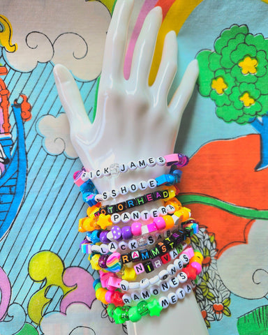 Stack of colorful lettered bracelets on a white plastic hand against a cartoon background