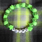 Green beaded bracelet with letter beads spelling 'METAL' on a plaid fabric background