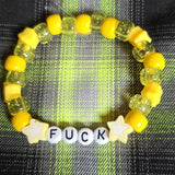 Yellow beaded bracelet with letter beads spelling 'FUCK' on a plaid fabric background
