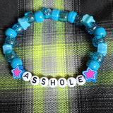 Blue beaded bracelet with letter beads spelling 'ASSHOLE' on a plaid fabric background