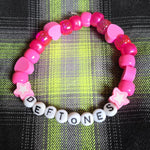 Pink and white beaded bracelet with 'DEFTONES' letters on a plaid fabric background
