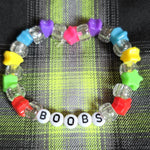 Colorful beaded bracelet with letter beads spelling 'BOOBS' on a plaid fabric background