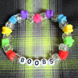 Colorful beaded bracelet with letter beads spelling 'BOOBS' on a plaid fabric background