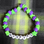 Green and purple bracelet with 'Misfits' beads on a plaid fabric background