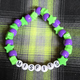 Green and purple bracelet with 'Misfits' beads on a plaid fabric background