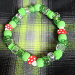 Green beaded bracelet with mushroom-shaped beads on a plaid fabric background